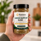 A hand holding a clear plastic jar of Nutrew Cardio Support Blend herbal food supplement, with a blurred indoor background.