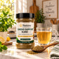 A jar of Nutrew Cardio Support Blend herbal food supplement sits on a kitchen counter next to a glass mug of tea, with a wooden spoon of loose herbal powder, fresh mint, and lemons in a bright, warm kitchen setting.