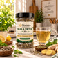 A jar of Nutrew Slim & Detox Tea herbal food supplement stands on a kitchen counter beside a glass mug of brewed tea, with ginger, mint, lemon, and other tea-related ingredients around it. The background shows a softly blurred kitchen interior.
