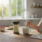 Person stirring a steaming cup of tea with a NuTrew product on a kitchen counter.