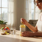 Woman pouring nutrew immunity booster into a jar on a table with fruits and a glass of water in the background.