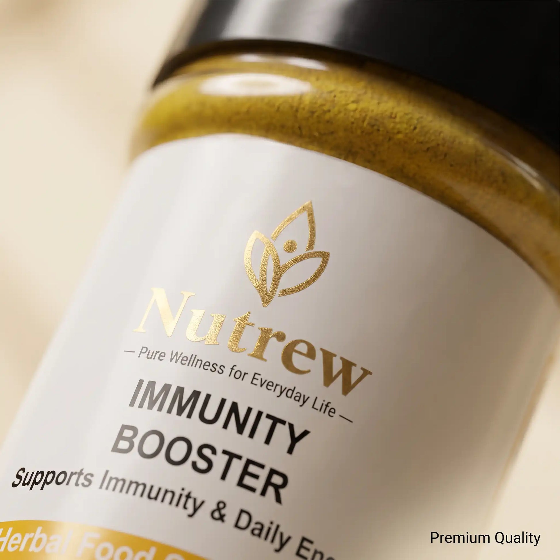 Close-up of a Nutrew Immunity Booster jar showing the white label with gold and black text, a gold powder visible at the top, and a black lid against a soft beige background.