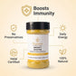 A bottle of Nutrew Immunity Booster herbal food supplement centered on a light beige background, surrounded by gold callout icons and text highlighting benefits: boosts immunity, no preservatives, daily energy, halal certified, and 100% natural.
