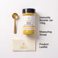 Nutrew Immunity Booster jar with a black lid, shown on a white background with a gold measuring scoop, a cream-colored product leaflet, and text labels reading 'Immunity Booster Jar 150g', 'Measuring Scoop', and 'Product Leaflet'.